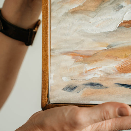 Person holding a framed abstract painting with soft colors