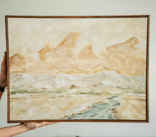 Person holding a framed landscape painting with mountains and water.