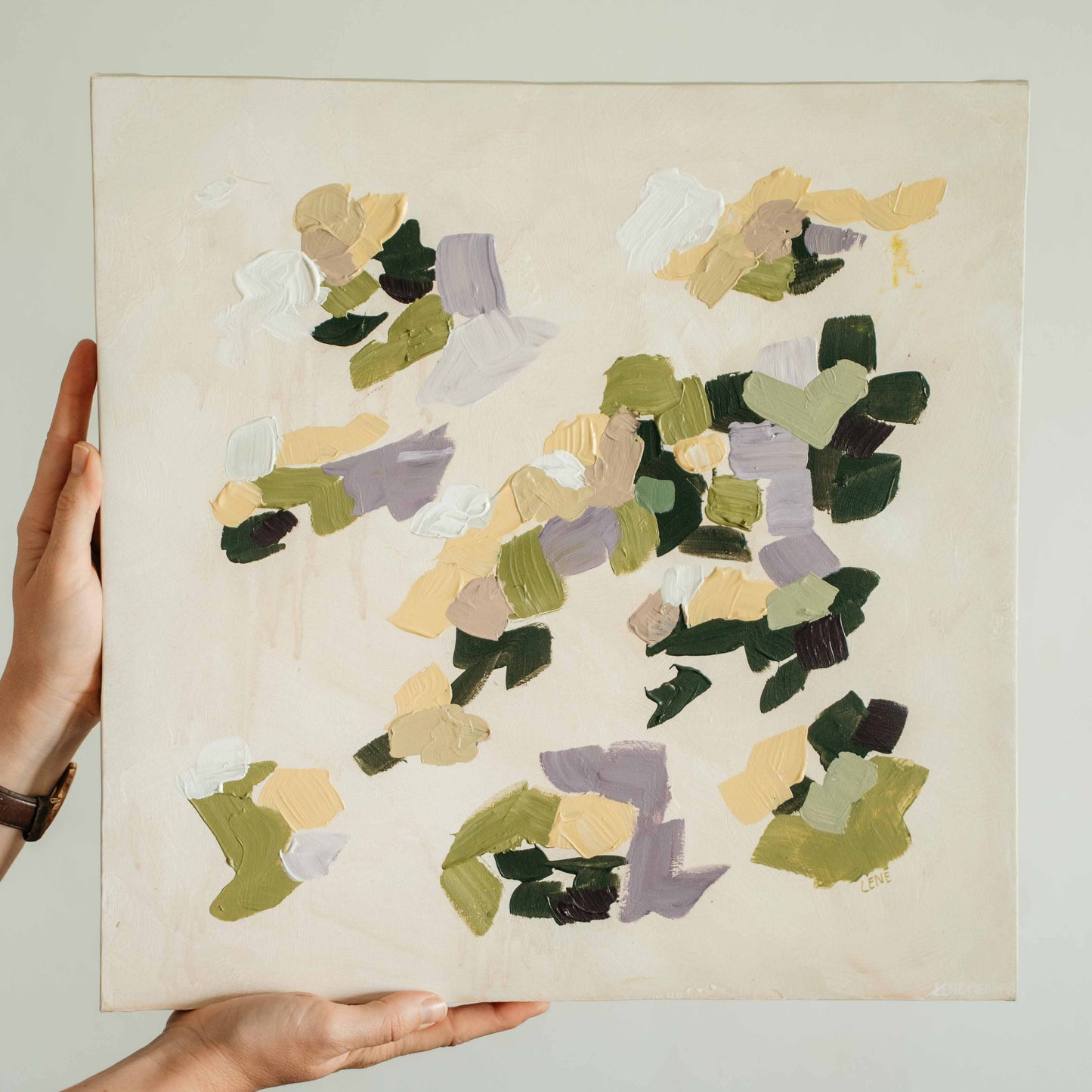 Hand holding an abstract square painting with abstract multicolored shapes on a beige background