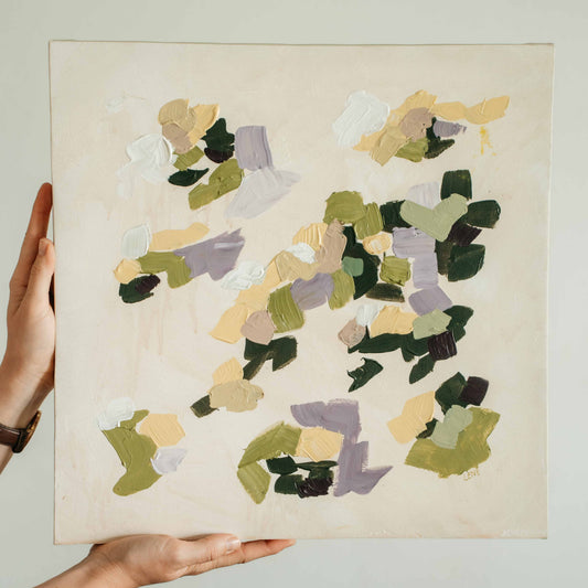 Hand holding an abstract square painting with abstract multicolored shapes on a beige background